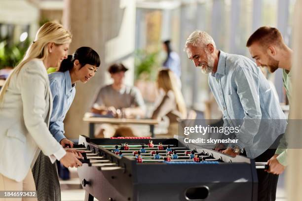Group of happy business colleagues having fun while playing table soccer on a break at casual office.